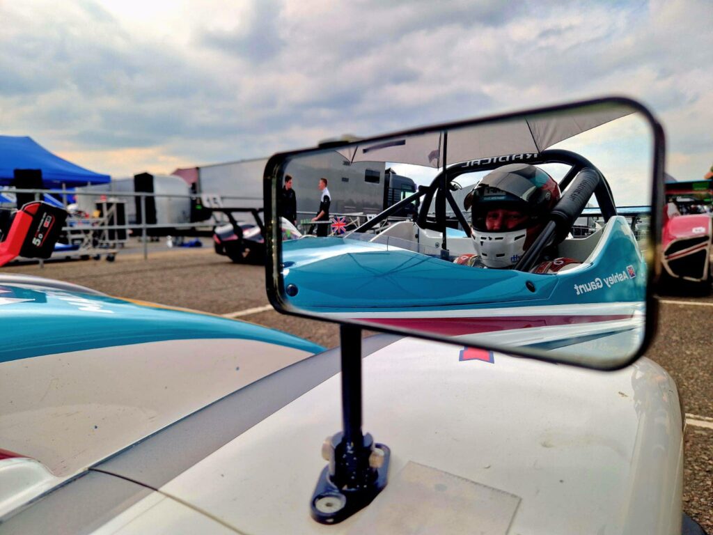 A Korniche and Made For Trade branded SR1 Racing Car with driver Ashley Gaunt visible through the car's mirror.