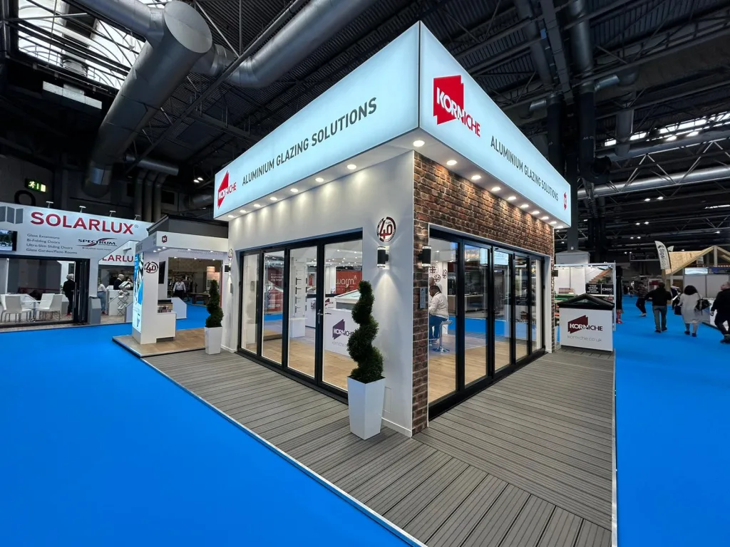 A pre-show view of the Korniche stand at the National Homebuilding & Renovating Show. The stand is set up with bi-folding doors, roof lanterns, and the new Flat Glass Rooflight System on display.