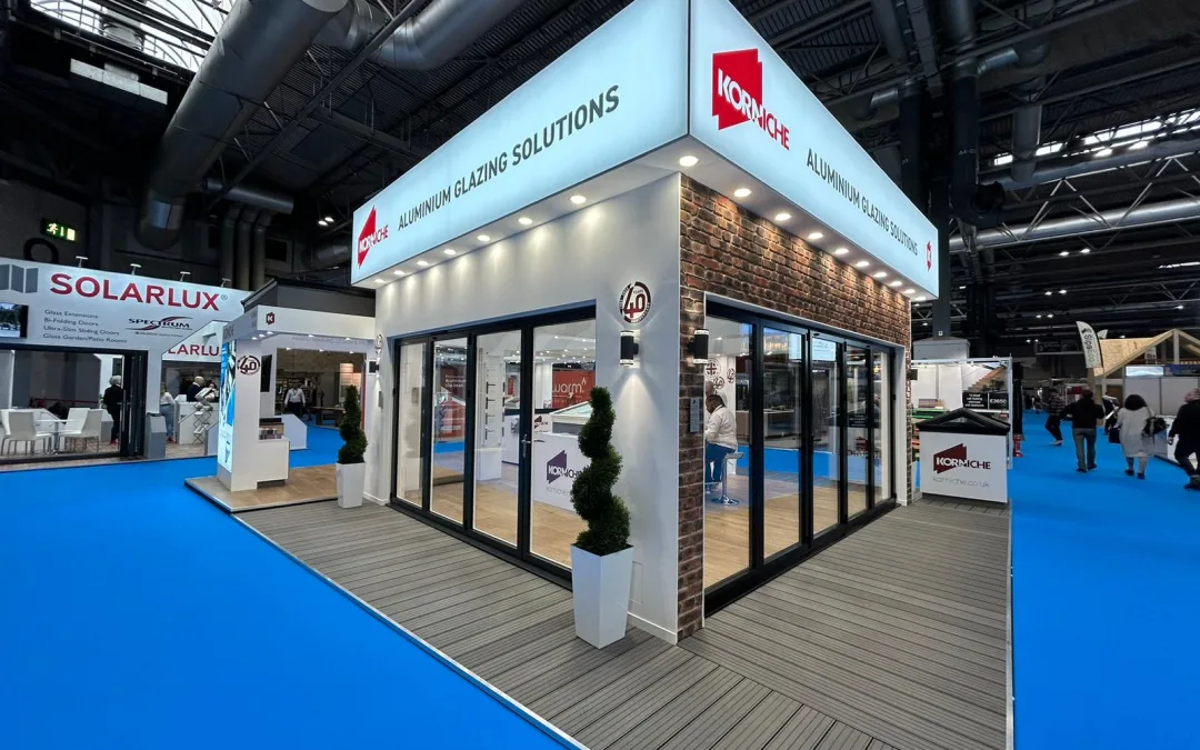 A pre-show view of the Korniche stand at the National Homebuilding & Renovating Show. The stand is set up with bi-folding doors, roof lanterns, and the new Flat Glass Rooflight System on display.