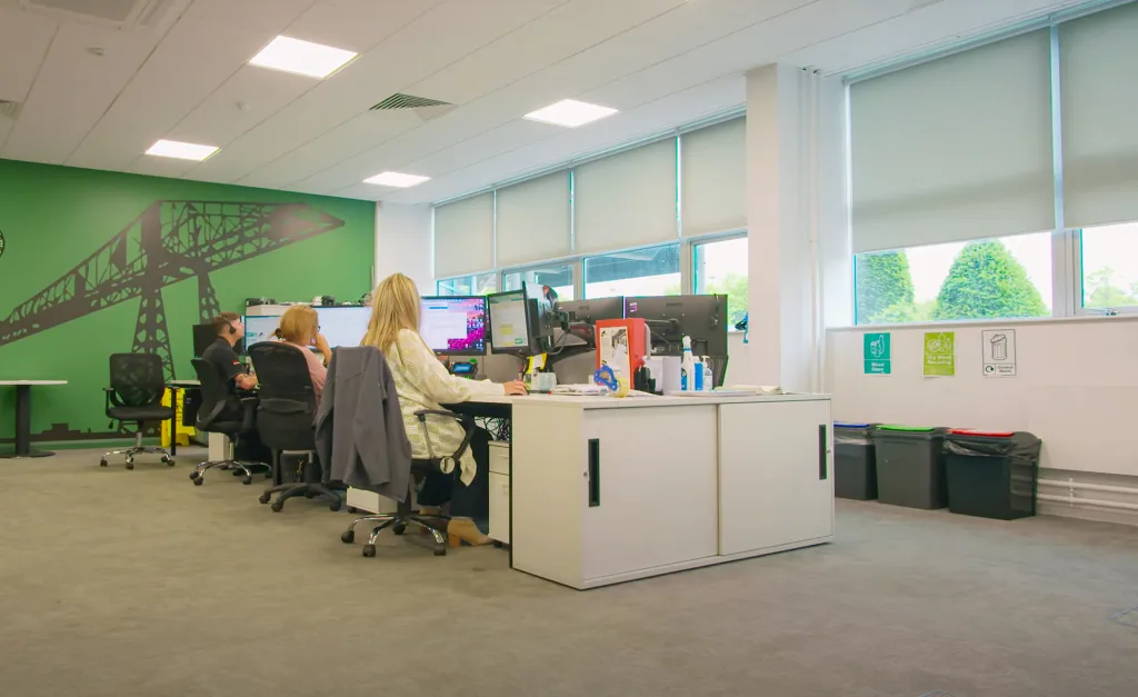 A photo of the Made for Trade customer service team working together in a bright office environment. Team members are smiling and talking on phones and headsets, with computers and customer files on their desks.