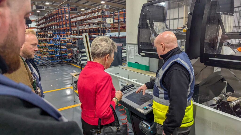 Factory Manager Frank Donaghy guiding His Majesty's Lord Lieutenant of County Durham, Mrs Sue Snowdon, through the Made For Trade factory, pointing at a CNC machine.